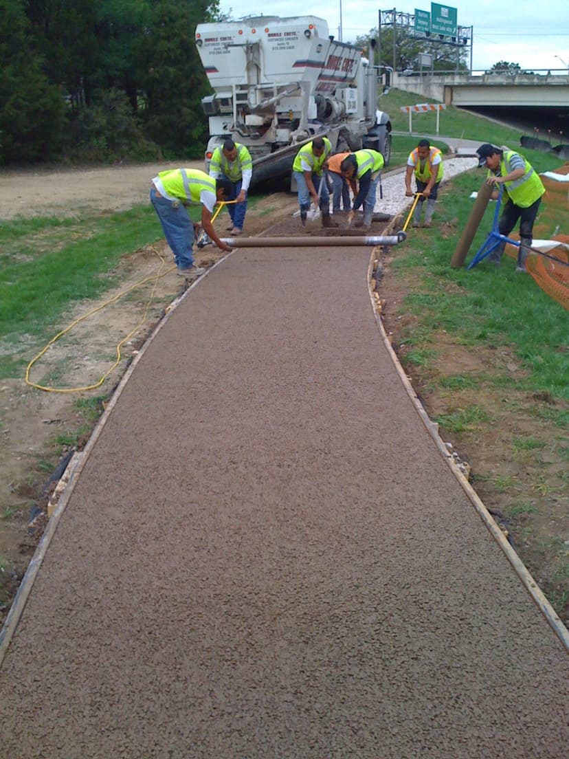 Construction crew pouring concrete for a walkway beside a highway.