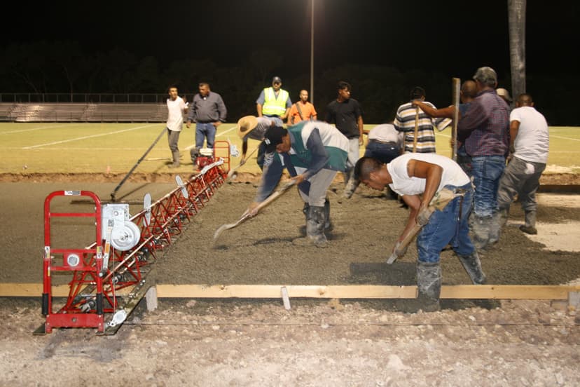 Construction workers pouring concrete at night for a sports field surface.